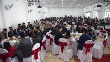 Un vaste espace de restauration intérieur, avec des tables rondes et des chaises blanches, dont certaines sont ornées de rubans rouges.