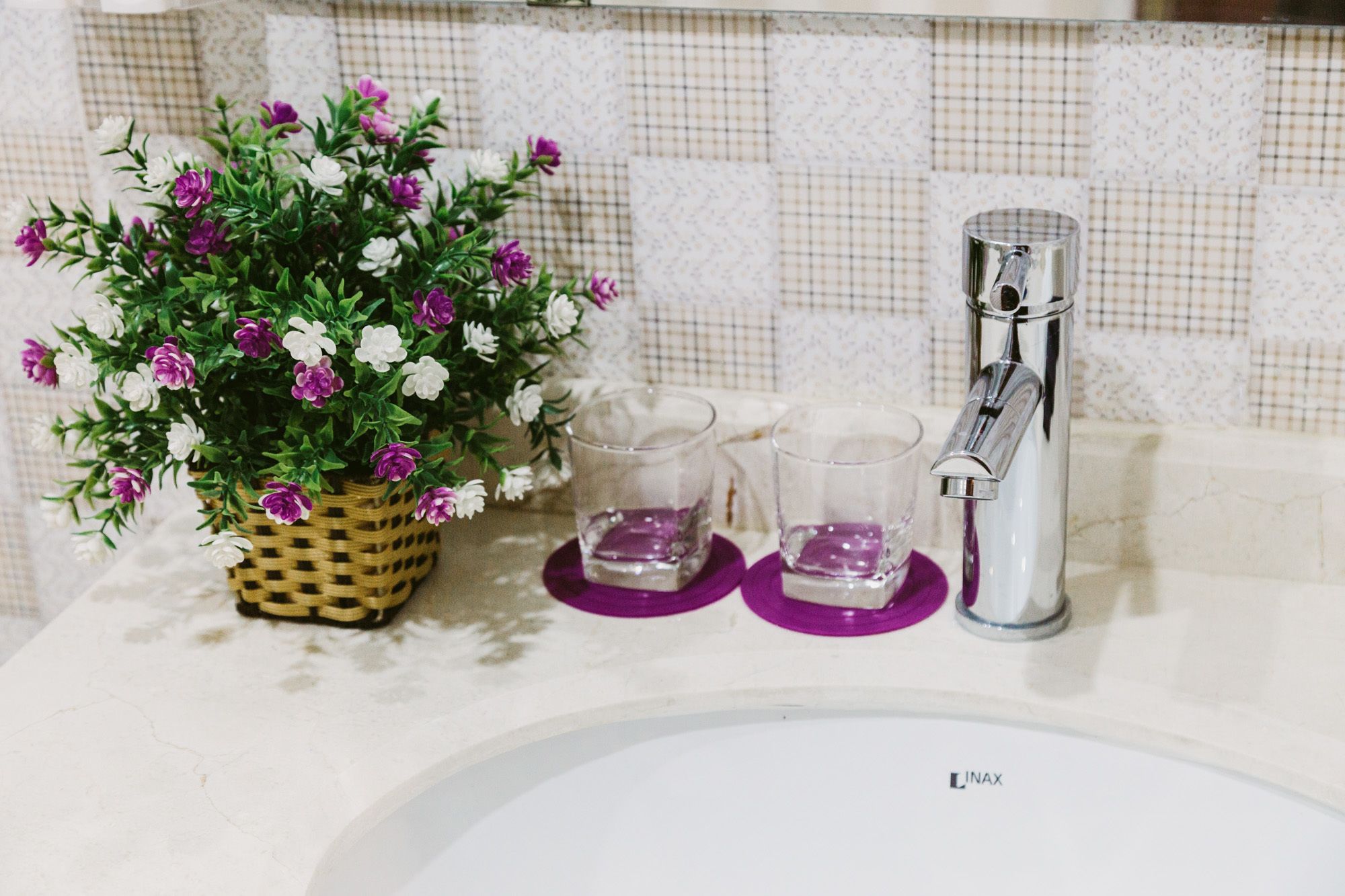 A bathroom sink with a faucet, a potted plant with flowers, and two glasses on a tray.