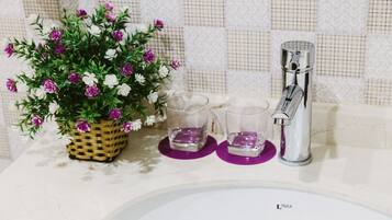 A bathroom sink with a faucet, a potted plant with flowers, and two glasses on a tray.