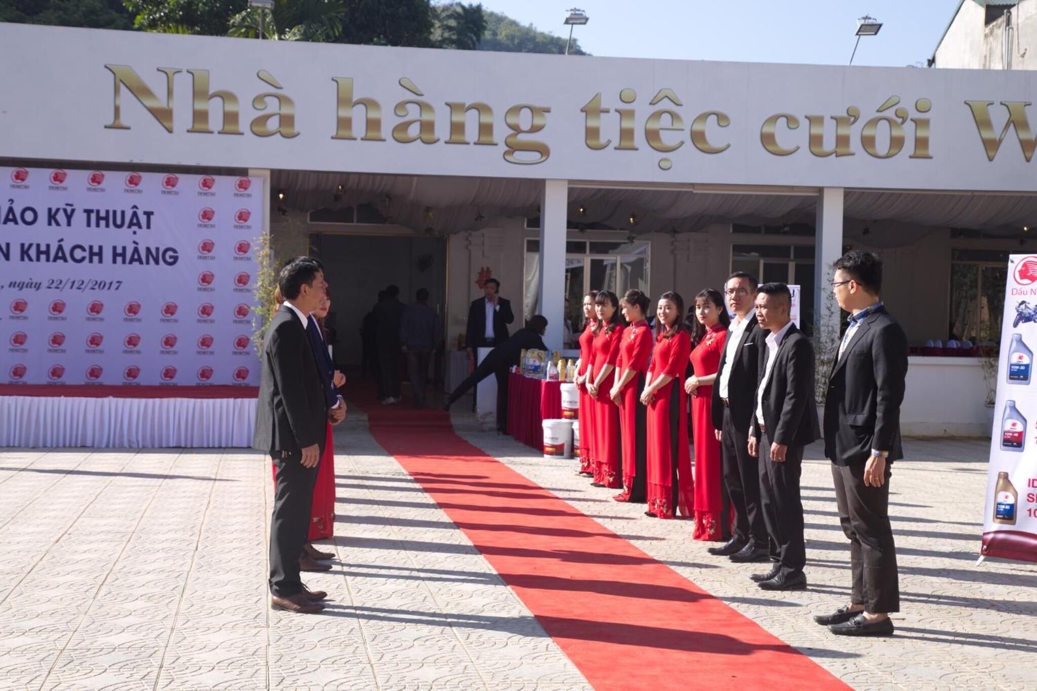 A group of people standing in front of a building with a red carpet and a banner with text.