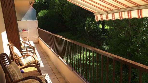 Varanda com mobiliário de vime, piso ladrilhado e vista para o verde.