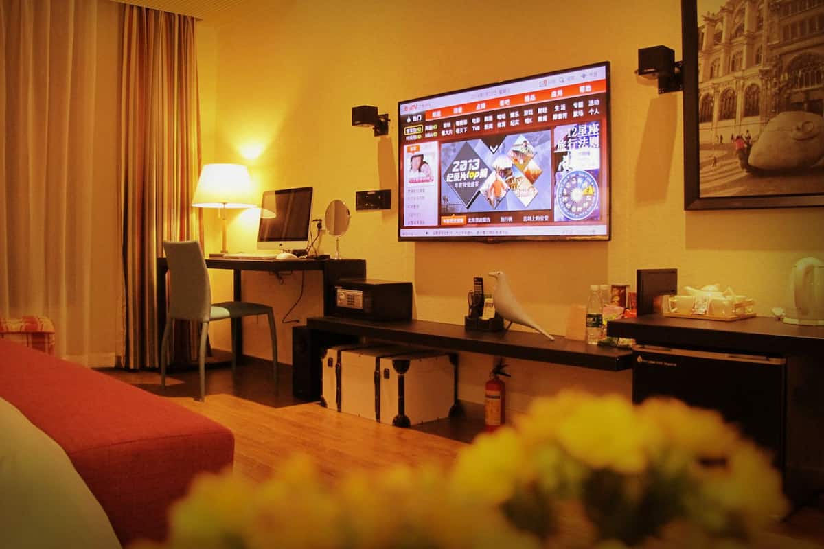 A hotel room with a bed, a desk with a computer, a TV mounted on the wall, and a fire extinguisher.