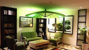 A living room with a green sofa, a coffee table, and a patterned rug. There are bookshelves filled with books and framed pictures on the walls. - Merrynest Hotel (Guangzhou)
