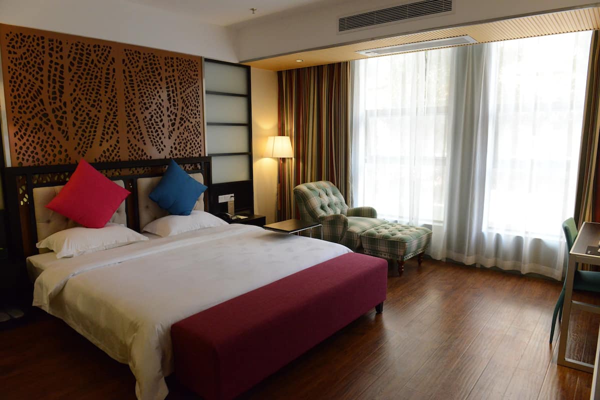 A hotel room with a large bed, a chair, a desk, and a window with curtains.