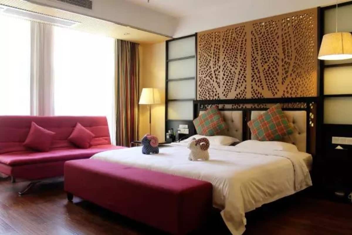 A hotel room with a bed, a red sofa, a small table, and a decorative wall panel.