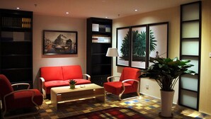 A living room with a red sofa, a coffee table, and a patterned rug. There are bookshelves and framed pictures on the walls. - Merrynest Hotel (Guangzhou)
