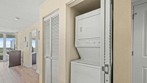 Une buanderie équipée d’un lave-linge et d’un sèche-linge, d’un placard avec porte coulissante et donnant sur le balcon.