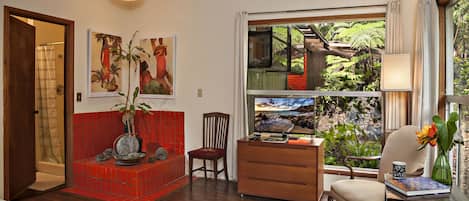 A room with a red tiled bench, wooden furniture, a desk with a computer, and a view of a staircase and greenery outside.