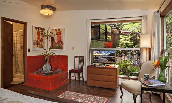 A room with a red tiled bench, wooden furniture, a desk with a computer, and a view of a staircase and greenery outside.