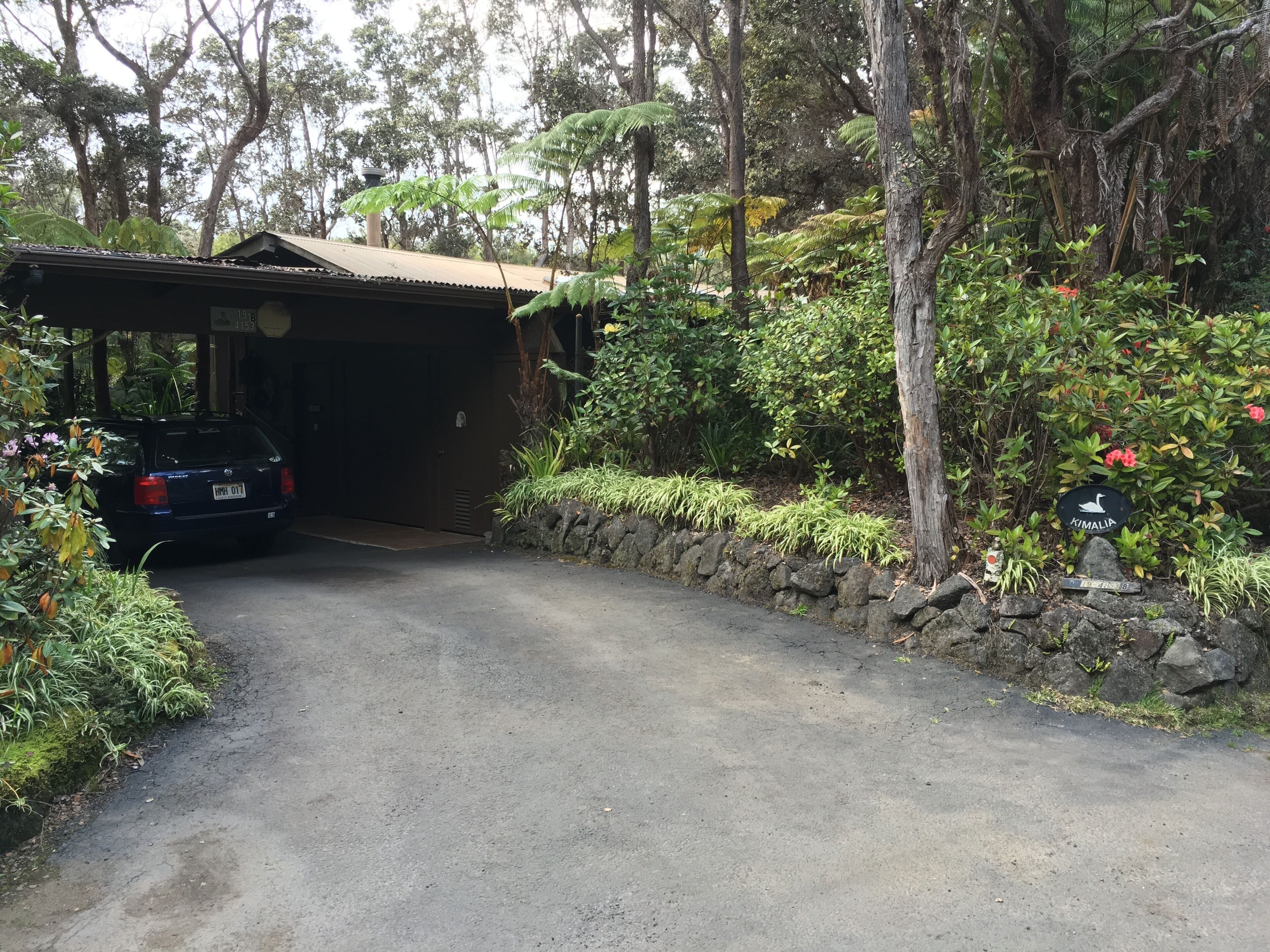 A parking area with a car, a covered structure, and lush greenery.