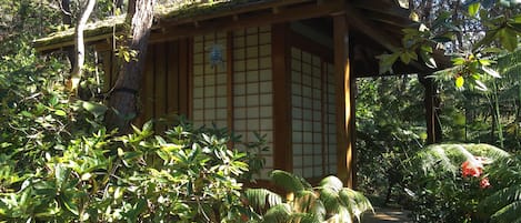 A traditional Japanese-style building with a wooden structure and sliding doors, surrounded by lush greenery and trees.