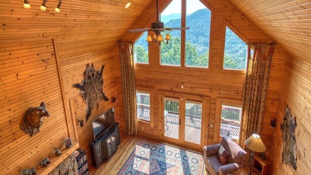 L’intérieur d’une cabane en rondins, avec une cheminée, un ventilateur de plafond, une grande fenêtre et une vue sur l’extérieur.