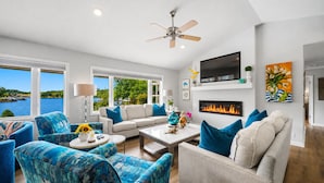 A modern living room with a fireplace, a ceiling fan, and a large TV. - "Bayshore Breeze" - Lakefront 7BR, Private Pool, Hot Tub, Putting Green, Views (Hot Springs)