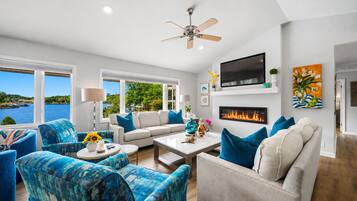 A modern living room with a fireplace, a ceiling fan, and a large TV.