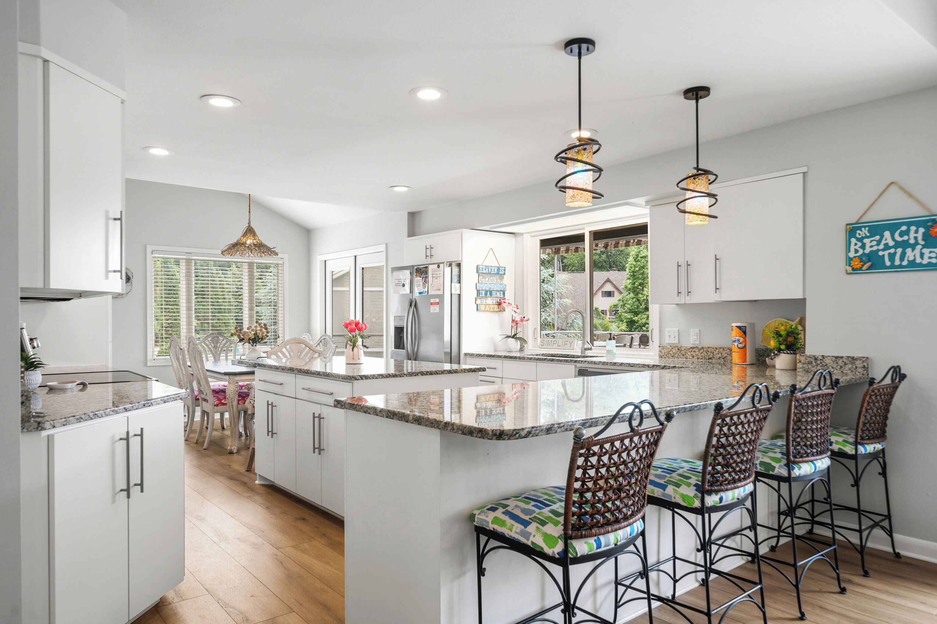 A modern kitchen with white cabinetry, a central island with bar stools, pendant lighting, and a view of the outdoors.