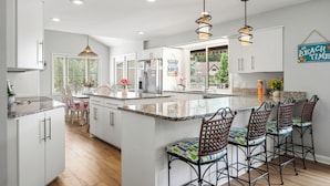 A modern kitchen with white cabinetry, a central island with bar stools, pendant lighting, and a view of the outdoors. - "Bayshore Breeze" - Lakefront 7BR, Private Pool, Hot Tub, Putting Green, Views (Hot Springs)