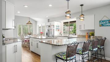 A modern kitchen with white cabinetry, a central island with bar stools, pendant lighting, and a view of the outdoors.