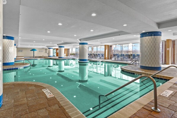 An indoor swimming pool with clear water, tiled walls, and a sunlit area with lounge chairs.