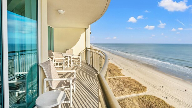 A balcony with a view of the beach, a table, and chairs. - Spacious Oceanfront Condo, Jacuzzi Tub, Lazy River | Mar Vista Grande - 1206 (North Myrtle Beach)