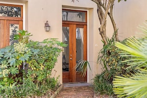 A house entrance with a wooden door, a small porch, and a brick pathway leading to the door.