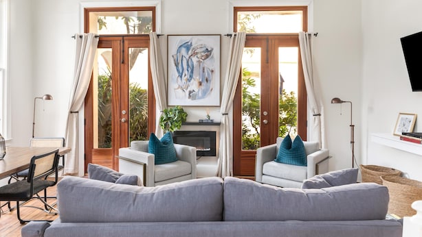 A modern living room with a grey sofa, two armchairs, a fireplace, and a large abstract painting. - French Quarter Escape – Walk to City Market, Rainbow Row & More (Charleston)
