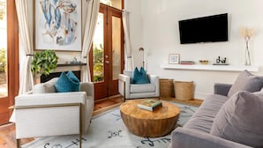A living room with a sofa, armchair, and coffee table. There is a TV mounted on the wall and a painting above the sofa. - French Quarter Escape – Walk to City Market, Rainbow Row & More (Charleston)