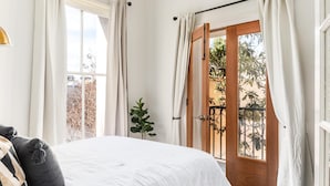 A bedroom with a bed, a window, a door, and a plant. - French Quarter Escape – Walk to City Market, Rainbow Row & More (Charleston)