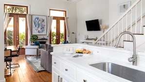 A modern kitchen with a large island, stainless steel sink, and a dining area with a table and chairs. - French Quarter Escape – Walk to City Market, Rainbow Row & More (Charleston)