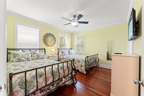 Un dormitorio con dos camas, ventilador de techo, televisor y cómoda.