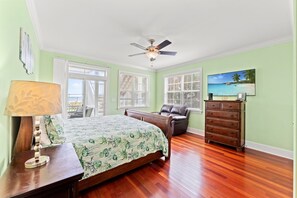 Une chambre à coucher comprenant un lit, une commode, un ventilateur de plafond et une fenêtre avec des stores.