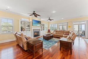 A spacious living room with leather sofas, a fireplace, and a large window overlooking a balcony. - Luxurious private beach house with private pool + Free Attraction Tickets! (North Myrtle Beach)