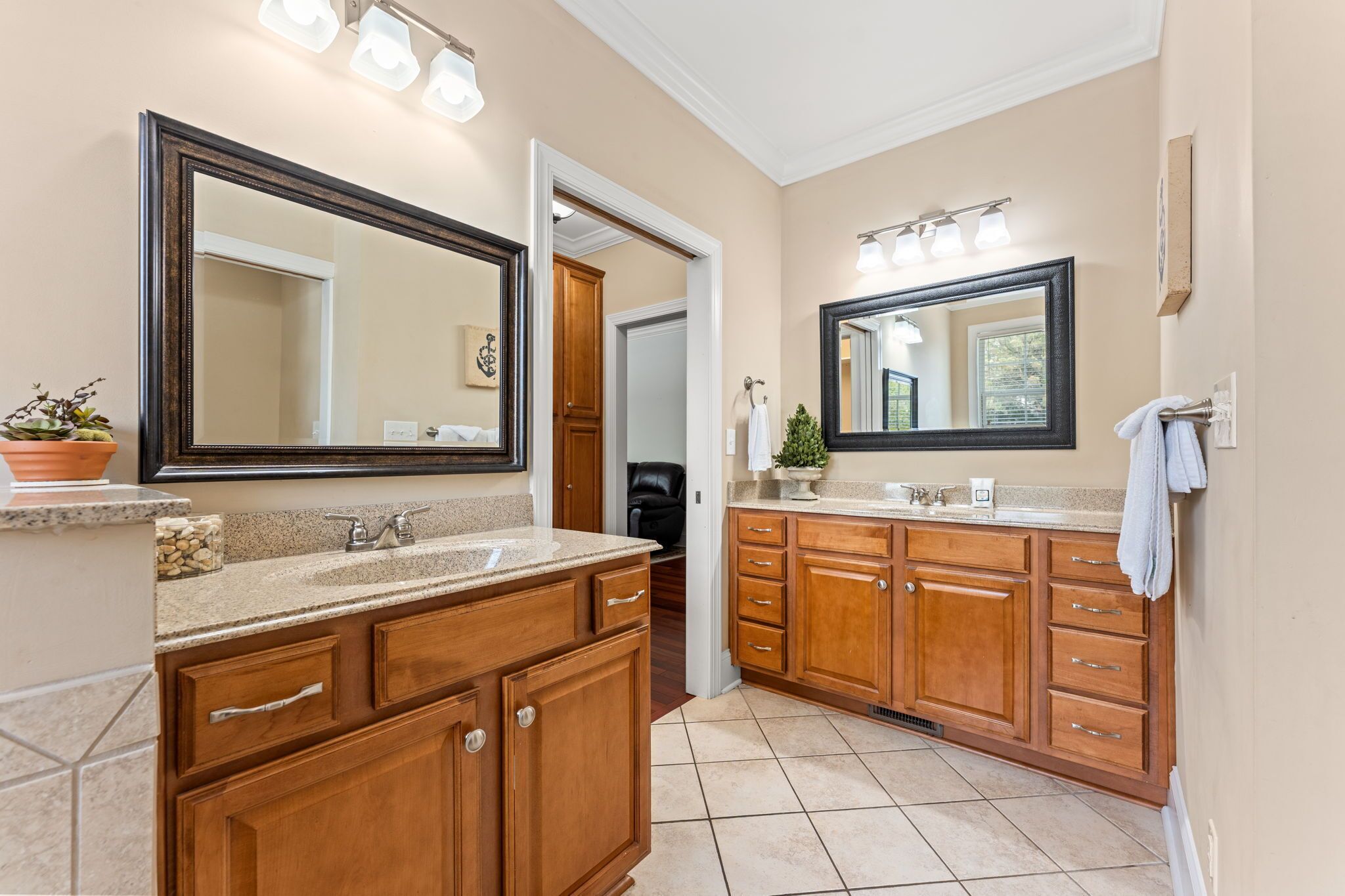 A bathroom with wooden cabinets, a granite countertop, a double sink, and a large mirror.