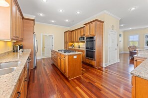 A spacious kitchen with wooden cabinets, granite countertops, a central island, and built-in appliances.