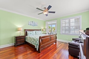 Un dormitorio con cama de madera, ventilador de techo, mesita de noche, cómoda y ventana con persianas.