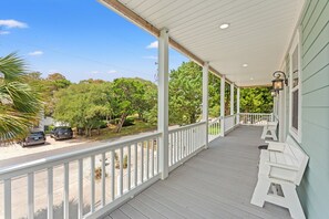 A covered porch with a railing, white benches, and a view of a street with parked cars and trees.