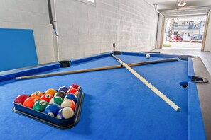 A pool table with balls and cues in a room with a brick wall and a garage door in the background.