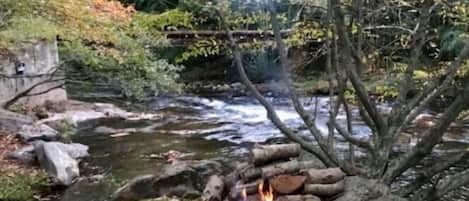 A riverside outdoor seating area with a fire pit and chairs.
