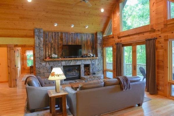 A log cabin interior with a stone fireplace, leather sofa, and a television.
