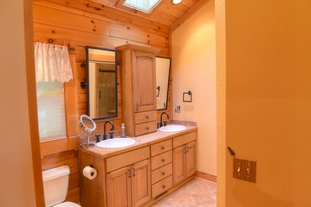 A wooden cabin-style bathroom with two sinks, a mirror, and a toilet.