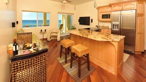 Una cocina con una isla grande, armarios de madera, un refrigerador de acero inoxidable y vistas al océano.