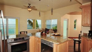 Una cocina con una isla grande, electrodomésticos de acero inoxidable, armarios de madera y vistas al océano.