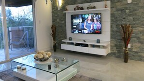 Una sala de estar moderna con una mesa de centro de vidrio, un televisor montado y una pared de piedra.
