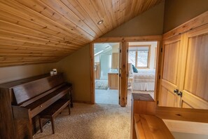 A cozy attic bedroom with a wooden ceiling, a piano, and a large wardrobe. - Stunning Home!  Rare Views & Ultimate Privacy – Perfect Location Bordering RMNP! (Estes Park)