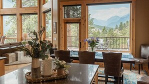 A spacious room with large windows offering mountain views, a dining area with a table set for two, and a cozy seating area with a sofa and chairs. - Stunning Home!  Rare Views & Ultimate Privacy – Perfect Location Bordering RMNP! (Estes Park)