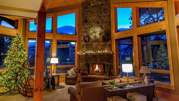 A cozy living room with a stone fireplace, large windows, and a Christmas tree. - Stunning Home!  Rare Views & Ultimate Privacy – Perfect Location Bordering RMNP! (Estes Park)
