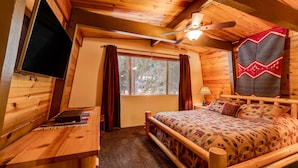 Een knus houten kamer met een bed, bureau en plafondventilator.