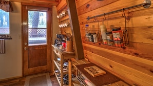 Een houten interieur met een keukenhoek, inclusief een houten deur, een raam en een plank met keukengerei en kruiden.