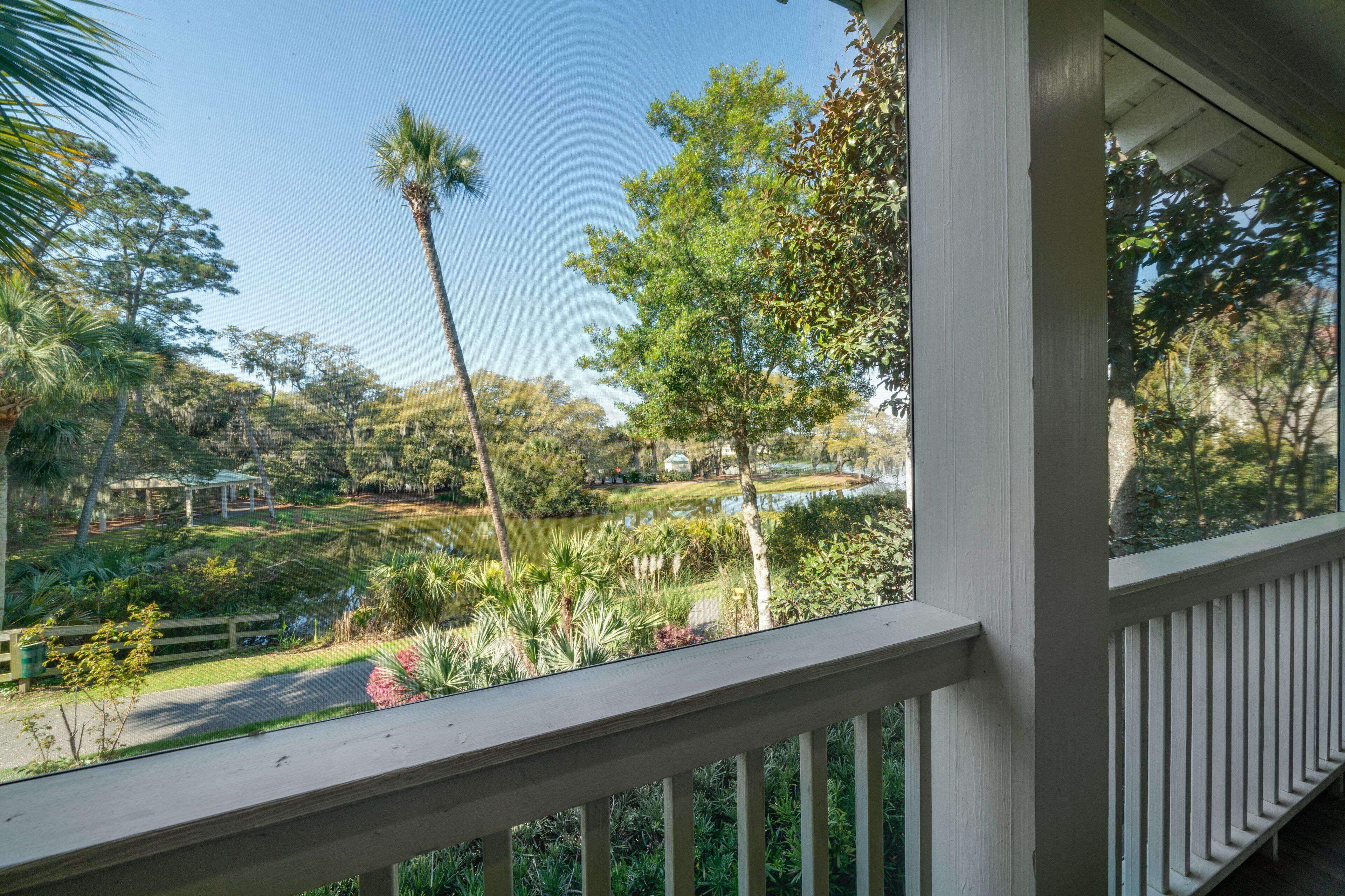 A view from a porch with a railing, overlooking a garden with a pond, trees, and a gazebo.