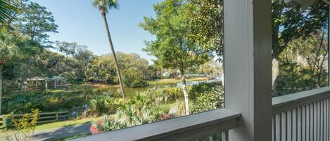 A view from a porch with a railing, overlooking a garden with a pond, trees, and a gazebo.