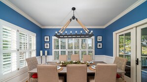 Une salle à manger avec une table dressée pour six personnes, entourée de chaises en osier, d’un lustre et de tableaux encadrés accrochés aux murs.